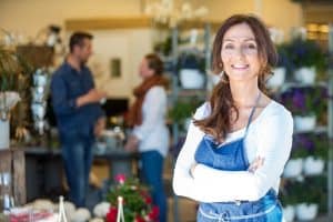 Portrait of smiling mid adult florist with customers in background at flower shop