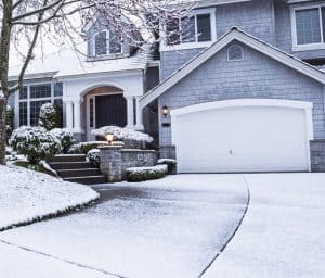 photo of suburban home with snow on drive way, lawn, plants, trees and roof