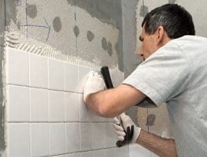 Man setting tile on cement board. He is tapping the tile in place with the handle of a hammer. Closeup. Real person on the job.