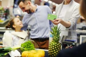 Woman giving plastic card to cashier while paying for food products at checkout