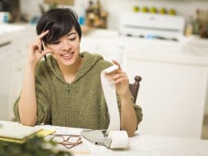 Multi-ethnic Young Woman Relieved and Smiling Over Financial Calculations in Her Kitchen.