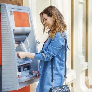 Young happy brunette woman withdrawing money from credit card at ATM