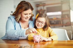 mother and daughter putting coins in a piggy bank at home