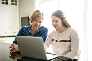 mother using a laptop in kitchen with teenager