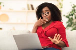 Shocking News. Amazed black woman watching something surprising on laptop, sitting on couch at home