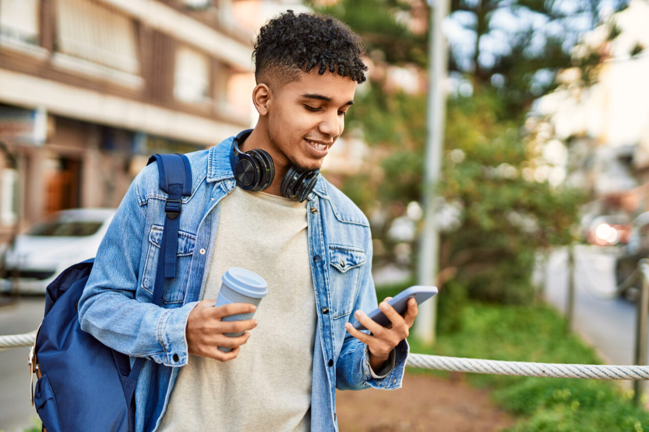 young man using smartphone to look up bank account, drinking coffee, on the go