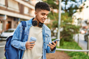 young man using smartphone to look up bank account, drinking coffee, on the go