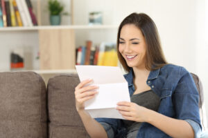 Happy woman reading a letter sitting on a couch in the living room at home