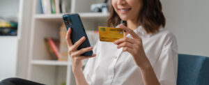 Happy young woman holding credit card and using smartphone for shopping online